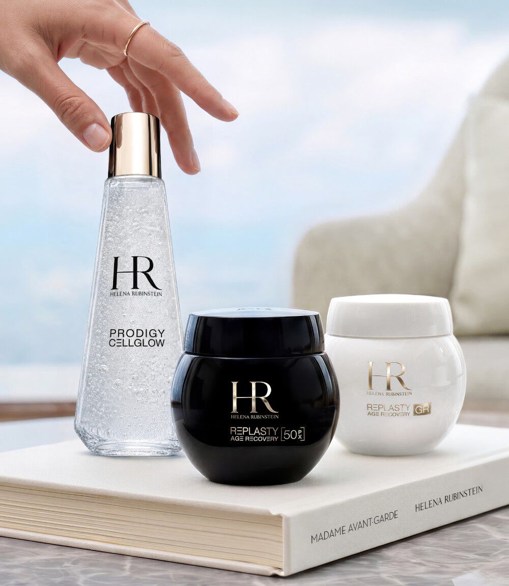 Drie huidverzorgingsproducten van Helena Rubinstein (Prodigy Cellglow en Re-Plasty) op een wit boek voor een raam met uitzicht op een landschap.​