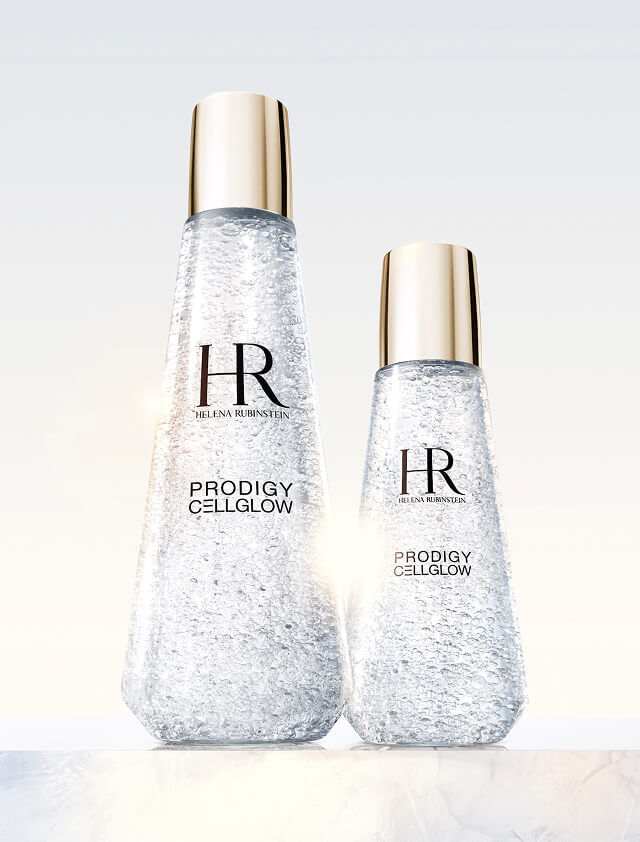 Twee transparante Helena Rubinstein Prodigy Cellglow serumflessen, een groot en een klein, gevuld met hydraterende belletjes en met gouden doppen, op een lichte achtergrond.