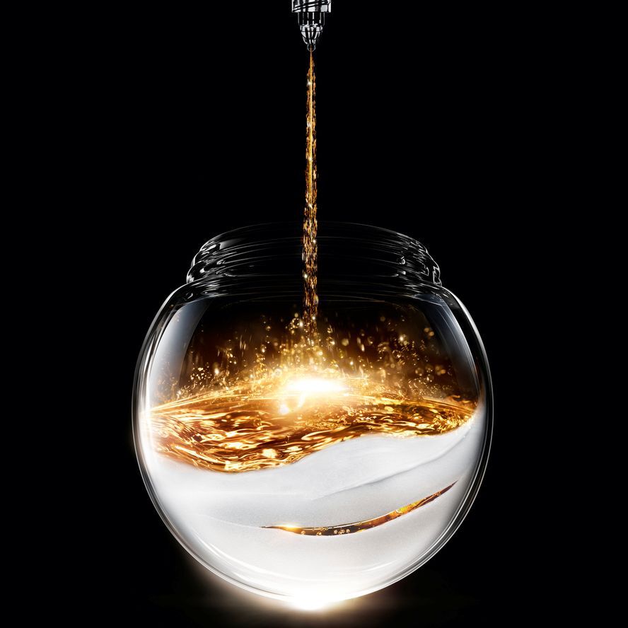 Sprankelende gouden vloeistof stroomt in een bolvormige glazen pot, rustend op een getextureerde witte basis, wat een lichtgevend contrast creeert op een zwarte achtergrond.