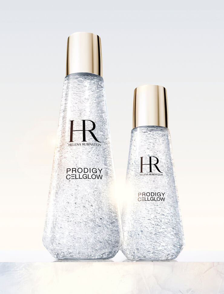 Twee transparante Helena Rubinstein Prodigy Cellglow serumflessen, een groot en een klein, gevuld met hydraterende belletjes en met gouden doppen, op een lichte achtergrond.