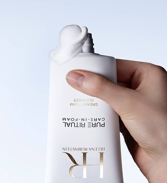 Een hand knijpt in een tube Pure Ritual Care-in-foam van Helena Rubinstein, waaruit een hoeveelheid product komt.