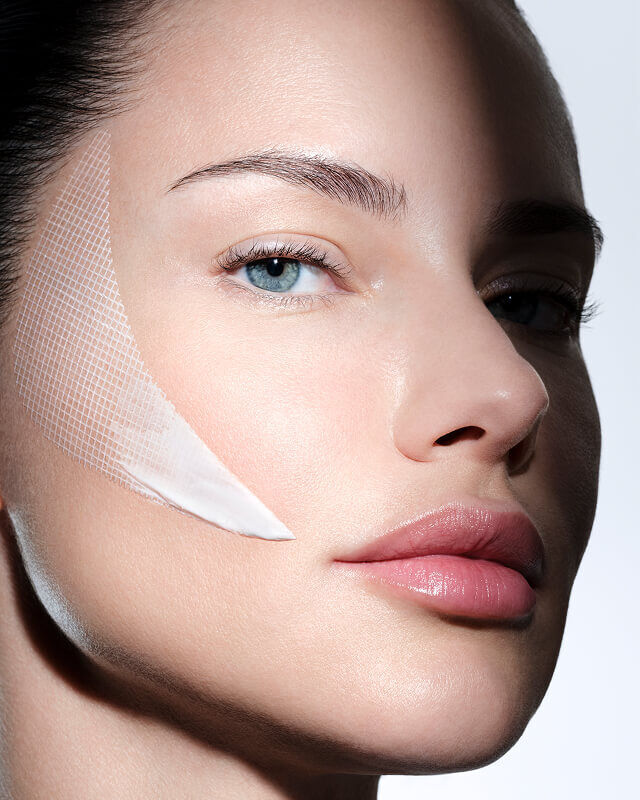 Gezicht van een vrouw met Helena Rubinstein REPLASTY creme en innovatieve bandage-textuur op haar wang.