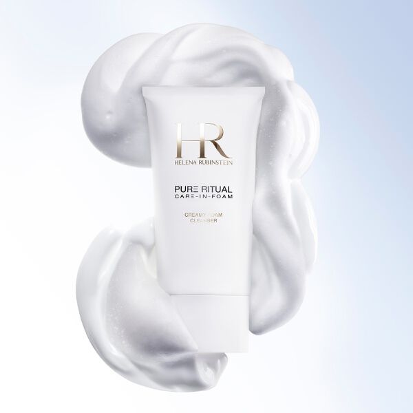 Close-up van de Helena Rubinstein Pure Ritual Care-in-Foam cleanser omringd door romig wit schuim, naast het gezicht van een vrouw met een zuivere en stralende teint.​