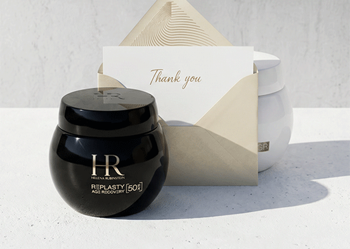 Een zwarte pot Helena Rubinstein Replasty Age Recovery-creme en een envelop met een 'Thank you'-kaart op een witte ondergrond, met een witte pot op de achtergrond