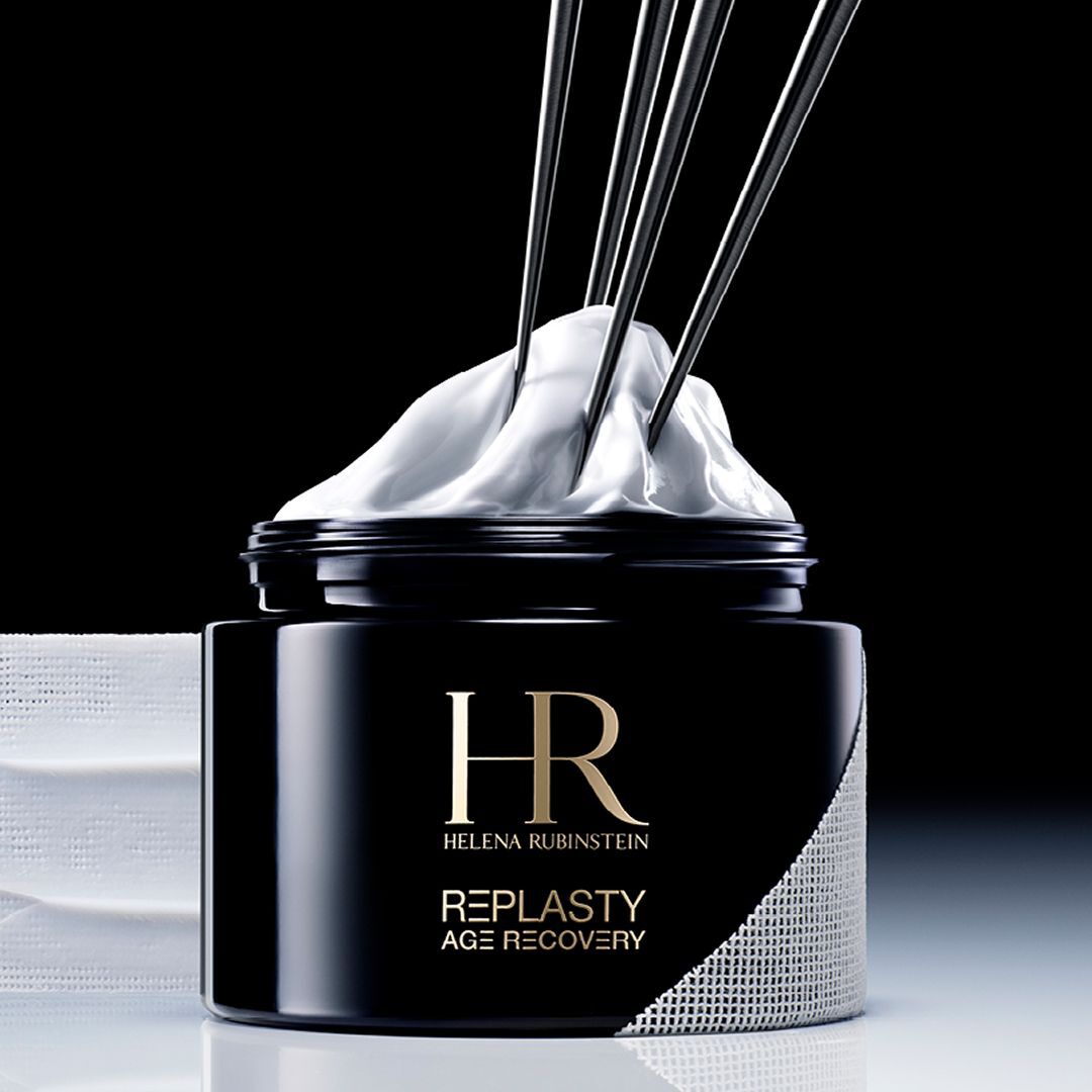 Helena Rubinstein Re-Plasty Age Recovery banner: Elegante zwarte cremepot, centraal geplaatst, met gouden reflecties en amberkleurige vloeibare elementen op de achtergrond. Donkere en luxueuze sfeer.