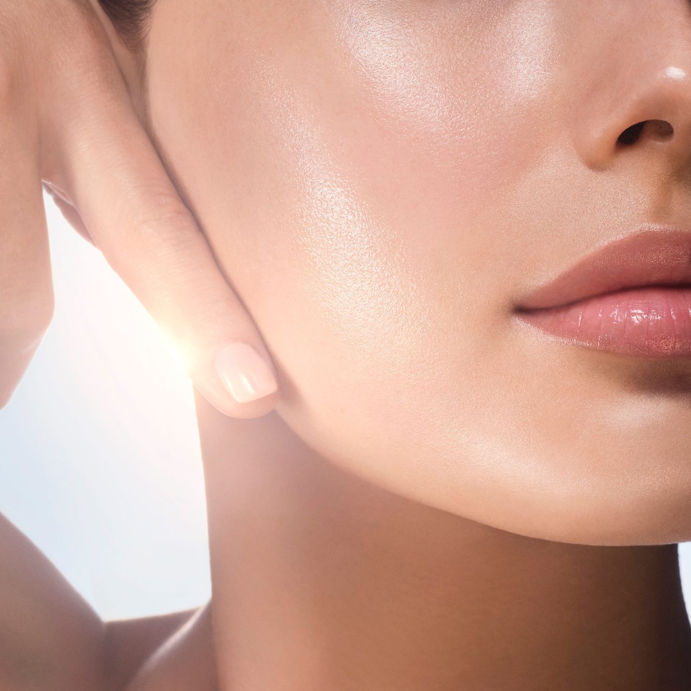 Heldere close-up van de gezonde, stralende huid van een vrouw, met een hand die zachtjes de wang aanraakt. Het licht benadrukt de gehydrateerde teint en roze lippen.