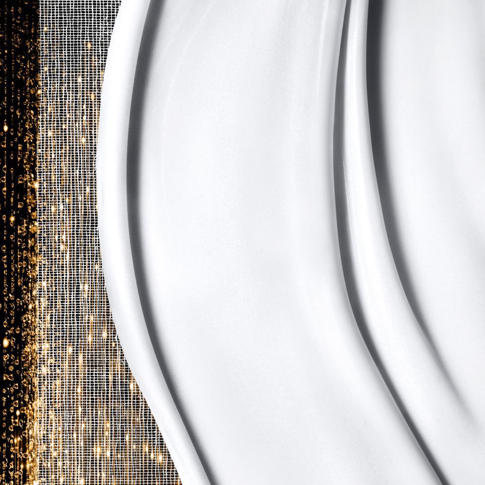 Gladde, romige witte textuur met zachte golven aan de rechterkant, naast sprankelende, abstracte gouden patronen aan de linkerkant.